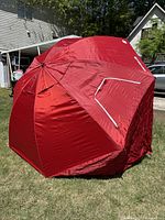 Large red sport shade umbrella fully opened outdoors on grass, showing shape, color, and side window panels.