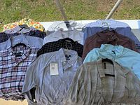 Full spread of 12 men’s dress shirts laid out on a flat surface outdoors, showing variety in color and pattern, hung on hangers.