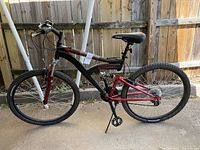 Side view showing the full suspension mountain bike with black and red aluminum frame, rear coil spring shock absorber, and knobby tires.