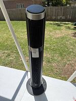 Full view of the tall black Dreo tower fan standing upright on a table outdoors, showing its height and slim profile.