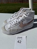 Side angle view of both white Nike high-top sneakers showing pink swoosh and toe detailing.