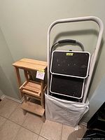 4 step stools grouped: wooden Ikea fixed-position step stool, two metal folding stools with black step surfaces and white frames, wooden folding stool, all shown leaning against the wall with plastic folding table