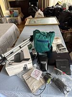 Overview of multiple electronics including tripod box, green bag, Sony Discman, portable DVD player, slide negative scanner, and accessories laid on table.