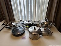 Overview of all pots and pans with lids arranged on table, showing different sizes and styles.