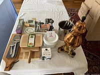Overview of entire lot on table including boards, plates, carafe, ice bucket, tongs, nutcracker, grater, boxed items