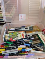Plastic container with an assorted collection of colored markers and pens, some pencils and brushes visible below.