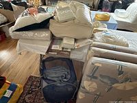 Lot displayed on table and floor with bedding and pillows stacked along with fold-up daybed visible beside them.