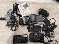 Overview of the lot showing multiple cameras, cords, manual, and case on a light carpet