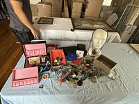 Wide shot of jewelry collection on table including jewelry boxes, colorful necklaces, pins, rings, and styrofoam display head
