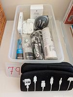 Top view of plastic tub showing earbuds by Apple, Sony, JVC, Apple adaptors, and black accessories case with cable icons.