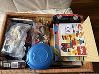 Photo of basket with plastic bags of LEGO pieces, LEGO boxes, plastic blue LEGO container, and red toy vehicle.