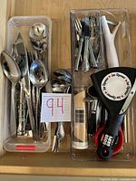 Photo showing trays with various metal serving utensils and kitchen tools including a garlic press, can opener, and jar opener.