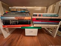Frontal view of stacked museum collections and Taschen art books on white shelf with faint lighting.