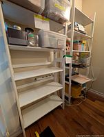 Photo showing two white wooden bookshelves side by side with four shelves each, placed against a wall on a hardwood floor. The bookshelves are empty with no items on shelves.