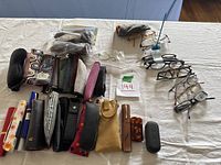 Photo showing multiple reading glasses laid out on a table, alongside numerous cases for glasses in various styles and colors.
