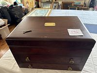 Closed rectangular dark wood storage case with brass key and brass hardware on front drawer section.