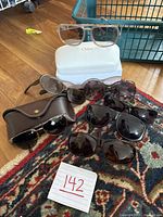 Overview of all sunglasses showing Chloe glasses in white case, Ralph Lauren in brown case, and other sunglasses arranged on carpet