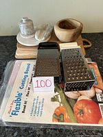 Photo showing all items including wooden cutting boards stacked, flexible cutting boards in packaging, two metal stand cheese graters, wooden bowl, marble salt cellar with spoon and butter dish.