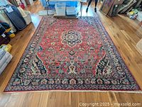 Full view of rug laid flat on hardwood floor showing red field and floral border