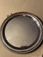 Top view of silver-plated tray showing detailed floral and shell pattern within the circular surface and twisted rope design on the rim.