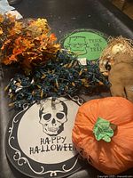 Photo of two scarecrow dolls, orange string lights, autumn leaves, and Halloween signs on a black table.