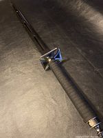 Close-up showing full-length black metal sword with textured handle on black background