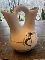 Front view of a white ceramic vase with two spouts and black feather design.