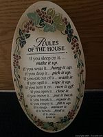 Oval white decorative wall sign with grapevine floral border and black printed family rules text.