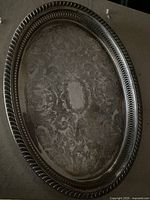 Oval serving tray showing ornate engraved pattern and braided edge design, tarnished.