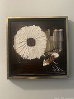 Close-up photo of one acrylic painting showing a large white flower with dark center on a dark background, framed in black frame with gold trim