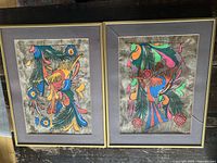 Two framed batik paintings side by side showing multicolored bird and floral designs, in gold-tone metal frames with gray mats.