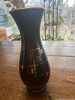 Full view of vase showing narrow base, flared rim with gold trim, and geometric multicolor patterns on black ceramic body.