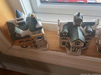 Two ceramic Christmas village houses with green and brown colored roofs and snow-like accents.