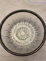 Top view of clear glass serving bowl with geometric pattern and dark tarnished silver rim.