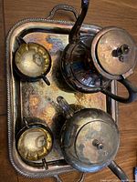 Bird's eye view photo showing all five items: teapot, coffee pot, creamer, sugar bowl, and tray with tarnished iridescent finish on wood background.