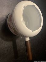 Top view of the fondue pot showing white metal with floral decoration and wooden handle.