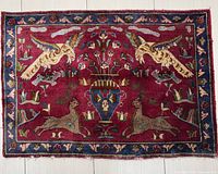 Full top-down photo of the Persian Mashhad rug showing the primary design of birds, deer, floral motifs on a deep red background with blue border.