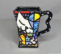 Front and side views of the ceramic mug showing the colorful abstract cat design and unique curved handle with white dots