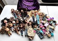 Wide view of assortment of Bratz dolls and accessories arranged on table with purple carry bag in background