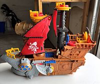 Side view of the Imaginext Shark Bite Pirate Ship showing shark-themed front, red sail with white emblem, yellow crow's nest, and seating area.