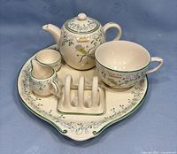 Overview of seven-piece breakfast set arranged on the serving tray showing the teapot, cup, cream jug, sugar bowl, and toast rack with decorative motifs.