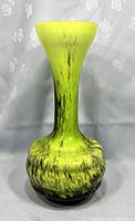 Front view of tall yellow and black speckled opaline glass vase with bulbous base and slender neck.
