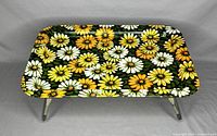 Top angled front view of metal lap tray showing floral design and foldable legs.