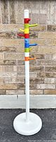 Full view of vintage Ikea Krokig coat stand, tall with multicolor hooks on white base and pole against brick wall.