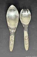 Pair of hammered silver plate salad servers with Kwakiuti carved handles side by side, showing condition and detail