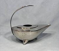 Side view showing the curved handle, pointed spout, and three triangular feet of the stainless steel kettle.