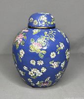 Front and angled views of a blue vintage Chinese porcelain ginger jar with a floral pattern in pink, white, and green. The jar includes a rounded lid and exhibits a glossy finish.