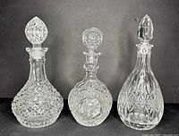 Front view of three vintage heavy cut crystal decanters with stoppers showing distinct patterns and designs
