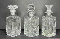 Front view of three vintage heavy cut crystal whiskey decanters showing detailed cut patterns and stoppers.