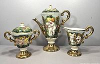 Front view of the vintage Italian Capodimonte coffee pot set showing intricate cherub designs, gold accents, and shapes of the coffee pot, sugar bowl, and creamer.